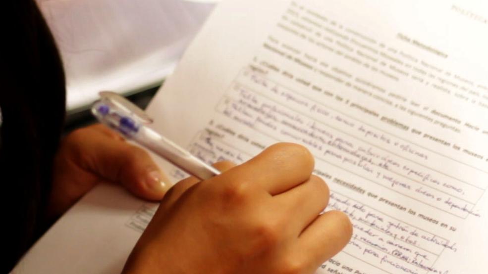 Mujer escribe sobre formulario en hoja blanca con lápiz azul.