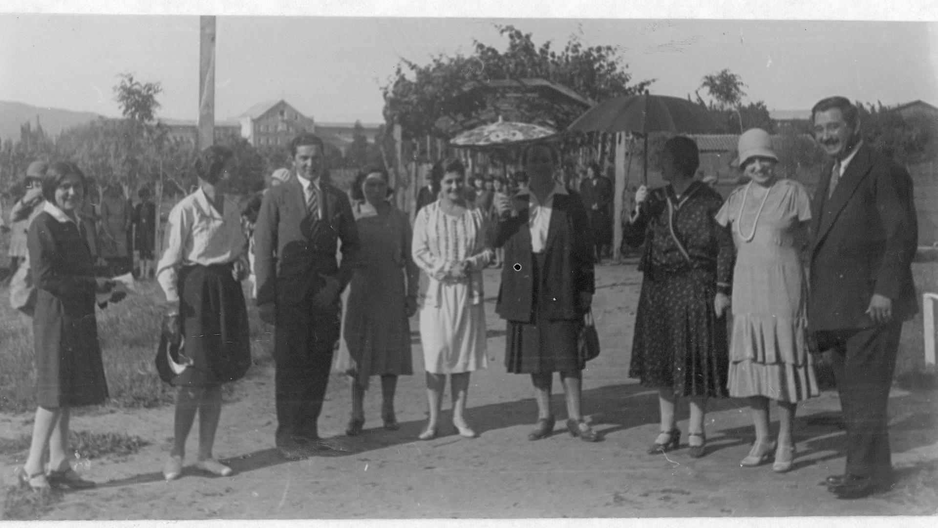 Grupo de hombres y mujeres en un balneareo, una de las mujeres lleva una sombrilla.