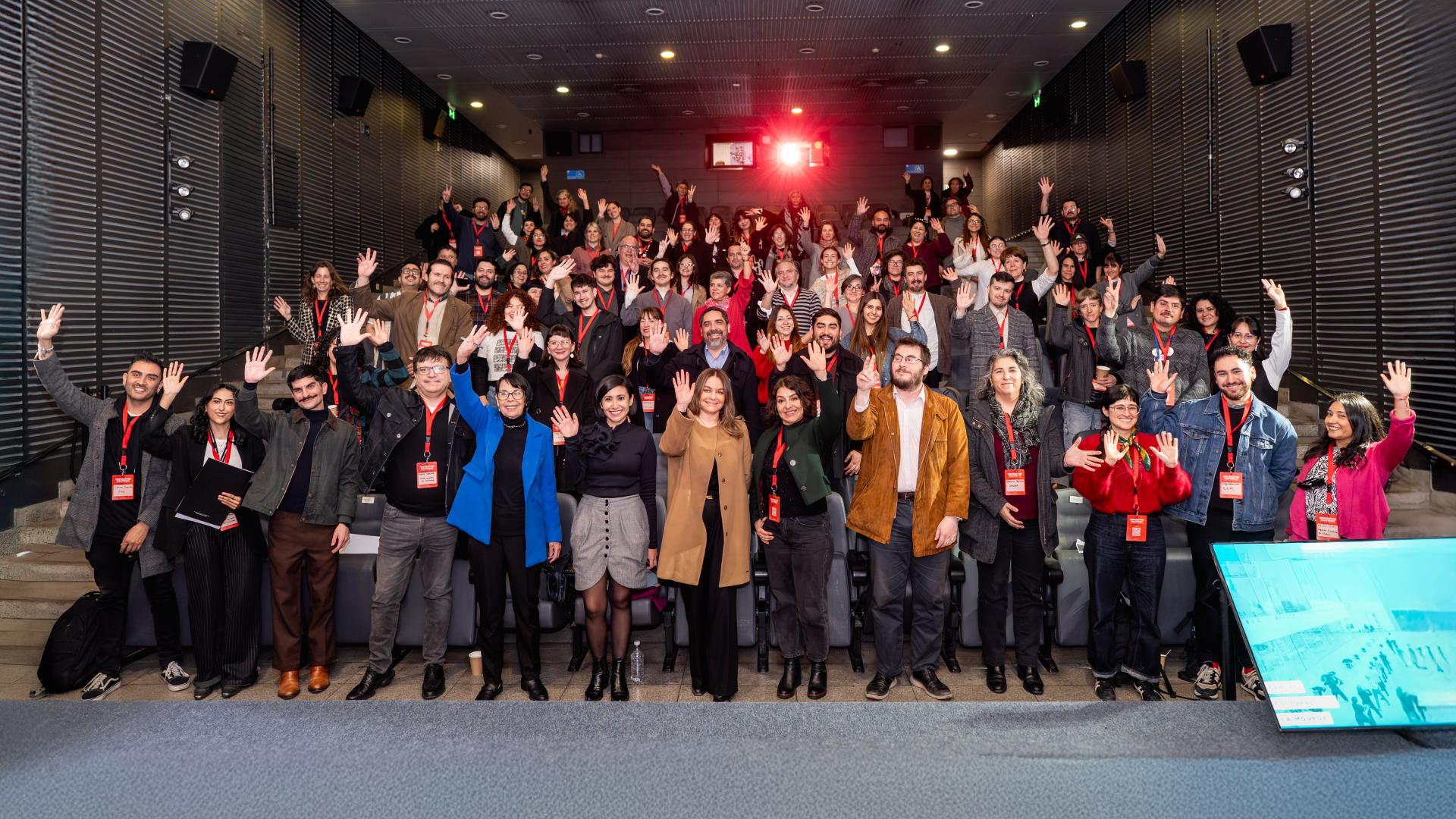 personas de pie en un teatro, saludan con la mano en alto