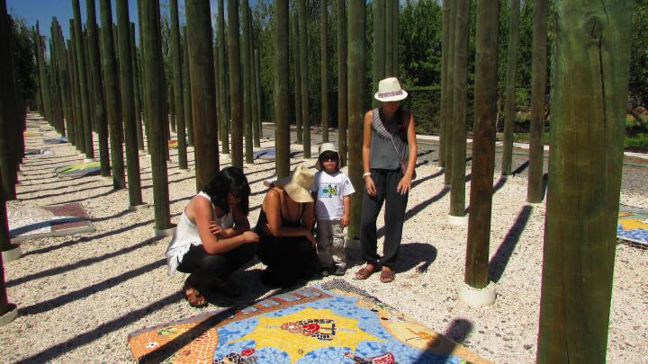 Grupo de personas observa un mosaico en el suelo, en medio de un bosque de varas de madera verde.