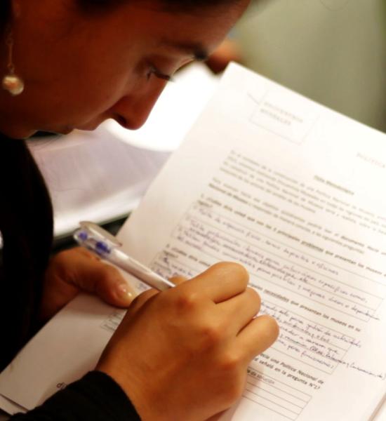 Mujer escribe sobre formulario en hoja blanca con lápiz azul.
