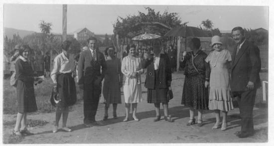 Grupo de hombres y mujeres en un balneareo, una de las mujeres lleva una sombrilla.